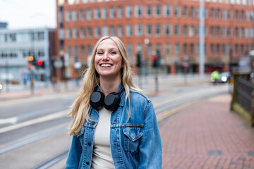 Smiling young woman walking in the city with headphones around her neck