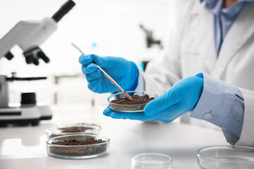 Scientist taking soil sample for research at white table in laboratory, closeup