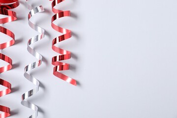 Shiny serpentine streamers on white background, flat lay. Space for text
