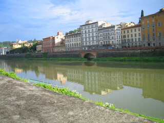 A tranquil view of the Arno River in Florence, Italy. Soft, natural light enhances the architectural beauty and symmetry of the scene, evoking a sense of timeless elegance and serenity in Florence.