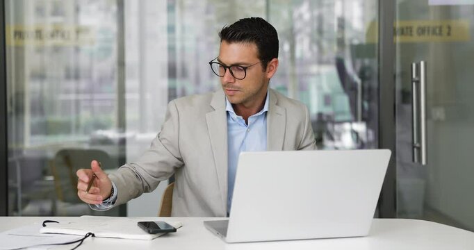 Smiling businessman working on laptop and writing important information, taking notes, making professional tasks, engaged in on-line educational learning, gains new skills seated at desk in workplace