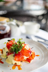 Gourmet smoked salmon with creamy sauce and greens on a white plate, served in an elegant setting with blurred teapot and cup in background
