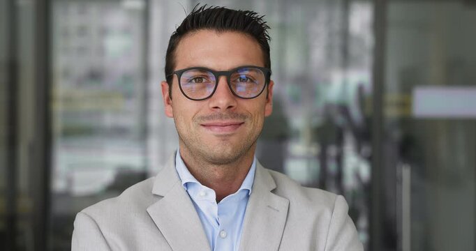Close up portrait of smiling professional Latin businessman dressed in formal suit wear glasses looking at camera with joyful expression, stands confidently in office, exuding competence and authority