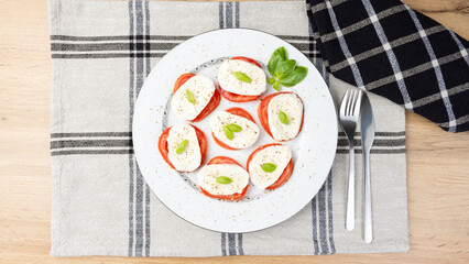 Overhead shot of a classic Caprese salad with mozzarella slices, tomatoes, and basil leaves on a white plate. Elegant food presentation on rustic napkin for culinary, editorial or menu use.