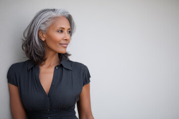 attractive Black woman with gray streaks in her hair against a plain  background looking to the right side
