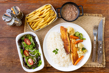 Prato Executivo Brasileiro Peixe filé de tilápia com Arroz, Batata Palha, feijão e Salada em Mesa de Madeira