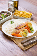 Prato Executivo Brasileiro Peixe filé de tilápia com Arroz, Batata Palha, feijão e Salada em Mesa de Madeira