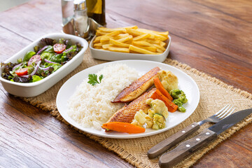 Prato Executivo Brasileiro Peixe filé de tilápia com Arroz, Batata Palha, feijão e Salada em Mesa de Madeira
