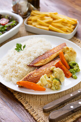 Prato Executivo Brasileiro Peixe filé de tilápia com Arroz, Batata Palha, feijão e Salada em Mesa de Madeira