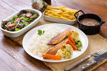 Prato Executivo Brasileiro Peixe filé de tilápia com Arroz, Batata Palha, feijão e Salada em Mesa de Madeira