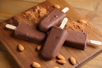 Four chocolate popsicles with almonds on wooden board