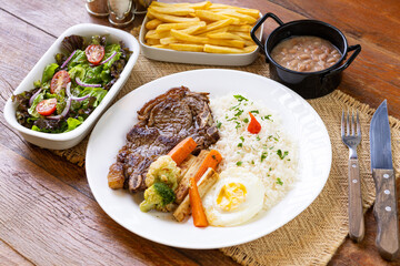 Prato Executivo Brasileiro de bisteca de boi com Arroz, Batata Palha, feijão, farofa e Salada em Mesa de Madeira