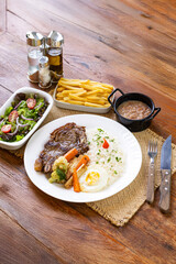 Prato Executivo Brasileiro de bisteca de boi com Arroz, Batata Palha, feijão, farofa e Salada em Mesa de Madeira