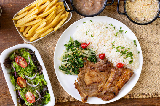 Prato Executivo Brasileiro bisteca de porco com Arroz, Batata Palha, feij&atilde;o, farofa e Salada em Mesa de Madeira