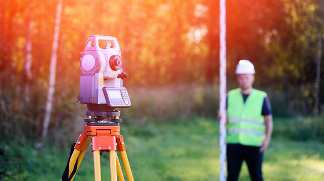 Surveyor engineer topographer with leveling rail on background of forest and tool for geodetic work. Total station and topographer cadastral engineer when performing cadastral work for land surveying.