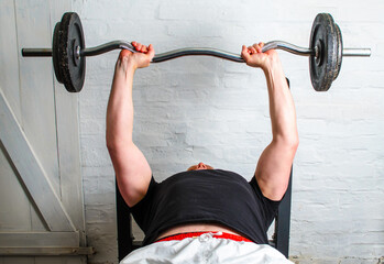 Man bench pressing barbell lying on bench in basement home gym workout