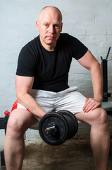 Man doing biceps curl with dumbbell sitting on bench in home basement gym
