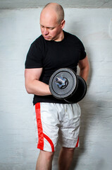 Man performing dumbbell biceps curls sitting on bench in basement gym
