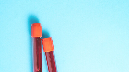 Two blood tubes with red liquid in them. The tubes are on a blue background. The tubes are next to each other