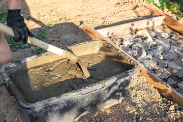Man with gloves mixing cement in a black tub with a shovel to build a foundation.