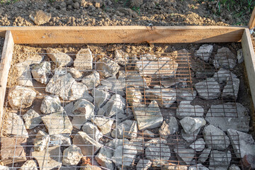 A construction site is prepared with rocks and wire mesh in a timber frame for pouring a concrete...