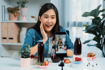 Smiling young beautiful Asian reviewing tasty mixed strawberry and cherry juice detox drinks,...