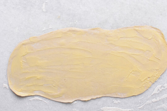 Overhead view of butter being spread on rolled out paratha dough, top view of flaky flatbread dough being covered with ghee, process of making paratha