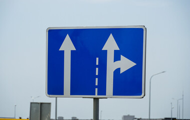 A blue traffic sign shows arrows directing vehicles straight ahead or to the right, positioned...