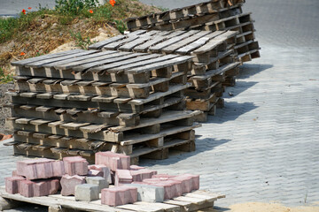 Wooden pallets are neatly stacked alongside colorful bricks on a paved construction site in bright...