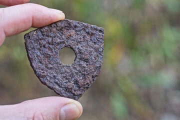 one brown iron small rusty plate with a hole lies on the palm of a hand in the street