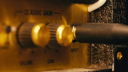 Close-up of plugging a jack into a guitar amplifier and turning up the volume knob, live concert show, playing music on guitar tube amplifier. - Powered by Adobe
