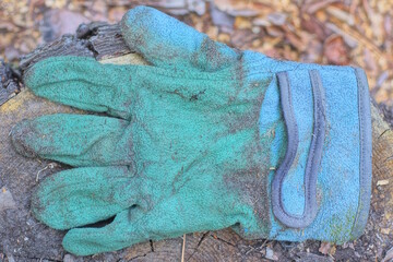 one old dirty blue green work glove lies on a gray wooden table on a summer street