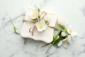 Soap bar and jasmine flowers on white marble table, flat lay