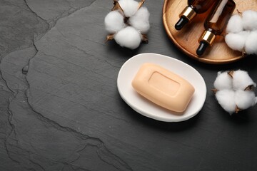 Soap bar, cosmetic products and cotton flowers on black table, flat lay. Space for text