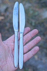 two old gray metal knives lie on the palm of a mans hand on a summer street