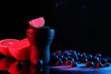 Hookah bowl with smoke and fruits on black table in neon lights, closeup. Space for text