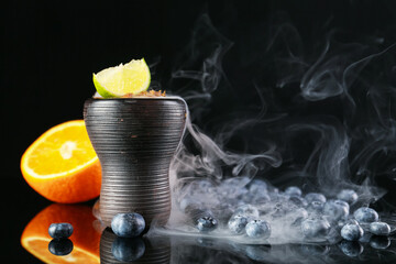 Hookah bowl with smoke and fruits on black table, closeup