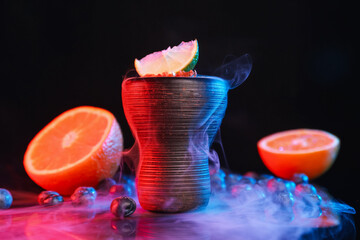 Hookah bowl with smoke and fruits on black table in neon lights, closeup