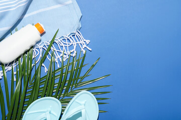 Beach accessories and palm leaves on blue background, flat lay. Space for text