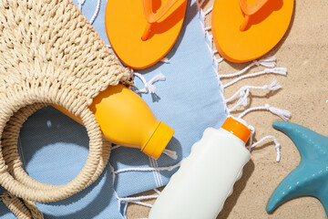Beach towel, sunscreen products, flip flops, wicker bag and sea star on sand outdoors, flat lay