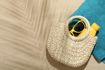Beach towel, straw bag, sunscreen product and sunglasses on sand outdoors, flat lay. Space for text