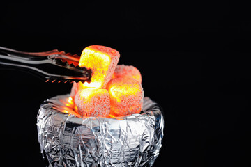 Putting smoldering charcoal cube into hookah holder covered with foil on dark background, closeup....