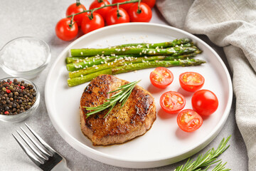 Close up, macro of tasty grilled beef steak served with green asparagus and cherry tomatoes on white plate, with cutlery. Perfect for food menu, diet, or culinary design concepts.