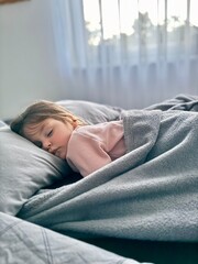 Adorable little girl is sleeping in the bed at home.