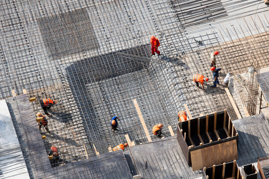 Construction workers assembling a rebar steel reinforcement cage at a bustling construction site, contributing to urban infrastructure development