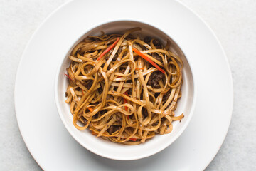 Overhead view of mongolian ground beef noodles in a white bowl, top view of ground beef noodles with scallions, green and red pepper