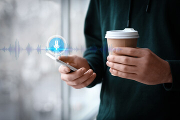 Young man with cup of coffee and modern mobile phone near window, closeup