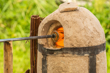 Glassblower or glassworker using a blowpipe and a glory hole to reheat a piece of molten glass with...