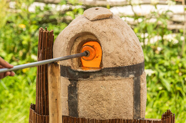 Glassblower or glassworker using a blowpipe and a glory hole to reheat a piece of molten glass with...