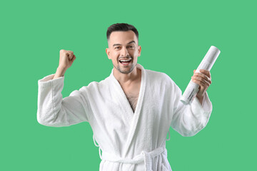 Happy young man in bathrobe with newspaper on green background